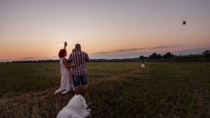 Diversity family with Samoyed watching yellow paper lantern fly through the sky at sunset.