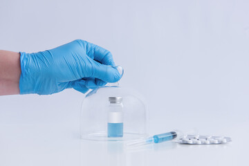 Fototapeta premium White isolated background stands the vaccine with syringe, pills. Doctors hand in blue medical glove