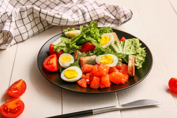 Plate of delicious salad with boiled eggs and salmon on white wooden background