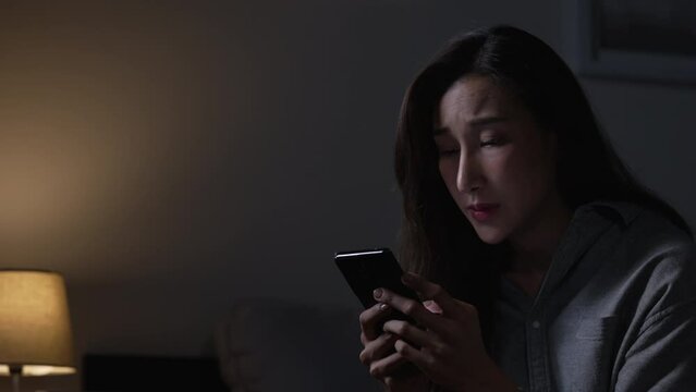 Exhausted young Asian woman using smartphone late at night.