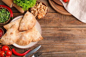 Plate with baked meat empanadas, meat, vegetables and herbs on wooden background