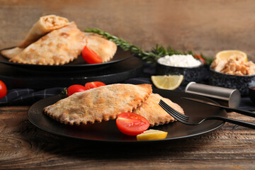 Plates with baked meat empanadas and tomatoes on wooden table, closeup