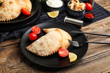 Plates with baked meat empanadas and tomatoes on wooden table, closeup