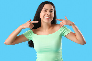 Fototapeta premium Beautiful young woman pointing at her smile on blue background