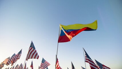 Flag of Venezuela waving in wind with many American flags on motion background on golden sunset with sun flare. National Venezuela flag visualizing independence, financial economy business partnership - Powered by Adobe