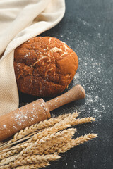 Homemade fresh bread, ears of wheat and a rolling pin on a black background, flat lay top view