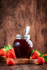 Strawberry jam in glass jar and fresh berries, rustic wooden table background, copy space