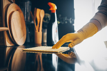 Closeup on woman's hands in yellow protective rubber gloves cleaning kitchen cabinets with sponge.