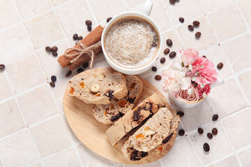Obraz na płótnie Canvas Board with delicious biscotti cookies, cup of coffee, flowers and beans on tile background