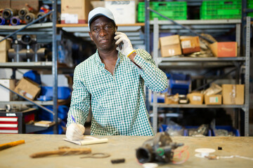 Portrait of African American man confirming order from customer at workplace in warehouse, talking...