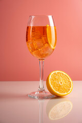 Glass of Aperol spritz cocktail on pink background.