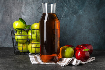 Glass bottle of fresh apple cider vinegar and basket with fruits on black grunge background