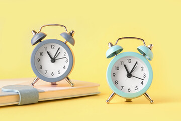 Alarm clocks and notebook on yellow background