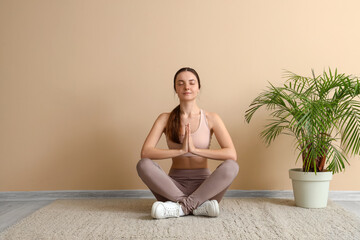 Meditating young woman sitting on floor near beige wall