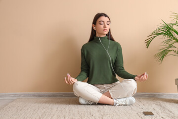 Meditating young woman sitting on floor near beige wall