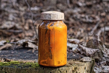 one old glass brown jar with yellow liquid stands on a gray stump outdoors in nature