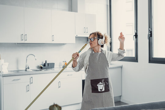 Carefree happy young woman cleaning house living room have fun dancing with mop, smiling overjoyed millennial girl feel excited enjoy making home chores sing entertain using floor broom or Swiffer.