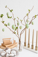 Vase with tree branches, Easter eggs, books and gift box on table near light wall, closeup