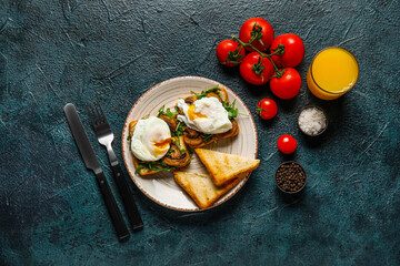 Plate with tasty eggs Benedict and glass of orange juice on black background