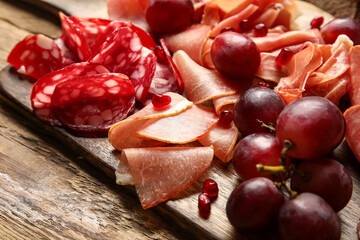 Board with assortment of tasty deli meats on wooden background, closeup