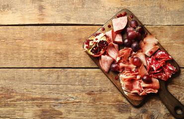 Board with assortment of tasty deli meats on wooden background