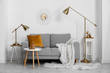 Cozy grey sofa with cushion, lamps and decorative pineapples on table near light wall