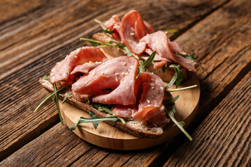 Board of tasty bruschettas with ham on wooden background