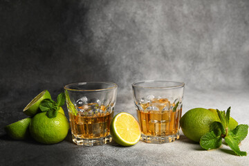 Glasses of rum with ice, mint and lime on grey background