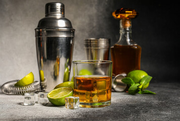 Glass of rum with ice, mint, lime and shaker on grey background