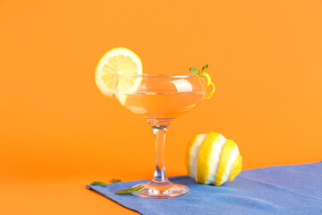 Glass of tasty martini and lemon on orange background