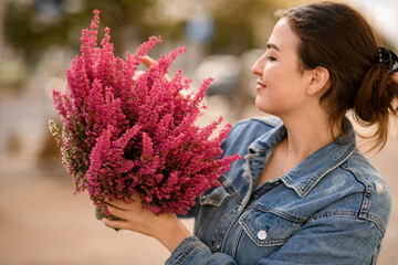 charming woman holds flower pot with flowering heather plant in the hands