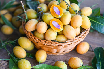 Marian plum fruit and leaves in basket on wooden background, tropical fruit Name in Thailand Sweet Yellow Marian Plum Maprang Plango or Mayong chid