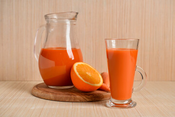 Fototapeta na wymiar Glass, jug of fresh carrot juice and oranges on light wooden table