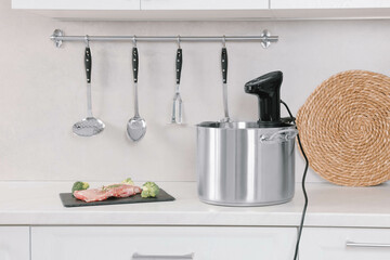 Pot with sous vide cooker and ingredients on table in kitchen. Thermal immersion circulator