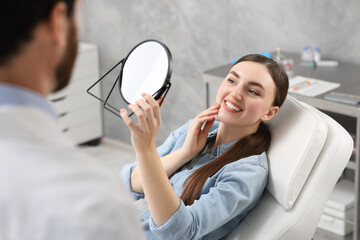 Young woman looking at her new dental implants in mirror indoors