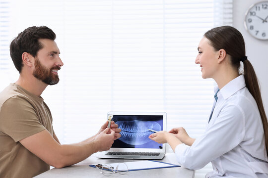 Doctor showing patient X-ray picture and educational model of dental implant in clinic
