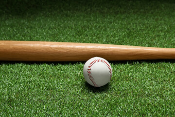 Wooden baseball bat and ball on green grass. Sports equipment