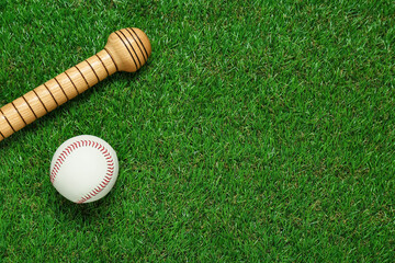 Wooden baseball bat and ball on green grass, flat lay. Space for text