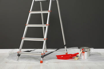 Metallic folding ladder and painting tools near gray wall indoors