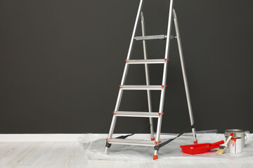 Metallic folding ladder and painting tools near gray wall indoors, space for text