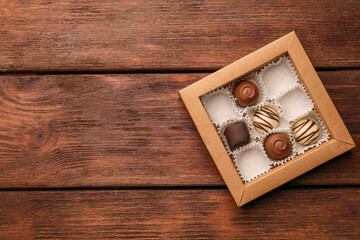 Partially empty box of chocolate candies on wooden table, top view. Space for text