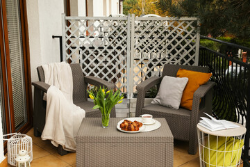 Different pillows, blanket, breakfast and beautiful tulips on rattan garden furniture outdoors