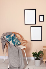 Empty frames hanging on beige wall, wicker chair and potted plant indoors