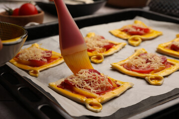 Spreading egg yolk onto raw puff pastry with tasty filling, closeup