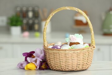Fototapeta na wymiar Wicker basket with painted eggs and delicious Easter cake near tulips on white marble table indoors
