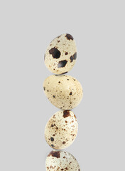 Stacked speckled quail eggs on light grey background