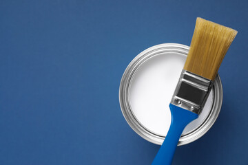 Can with white paint and brush on blue background, top view. Space for text