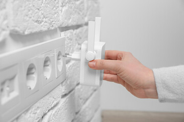 Woman inserting wireless Wi-Fi repeater into power socket indoors, closeup