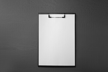 Clipboard with sheet of paper on black wooden table, top view. Space for text