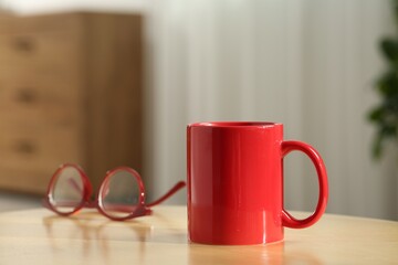 Red mug and glasses on wooden table indoors. Mockup for design